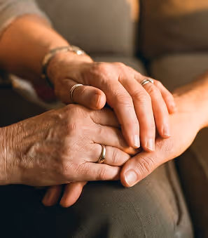 Close-up of two people holding hands, showing a comforting gesture with wedding rings visible.