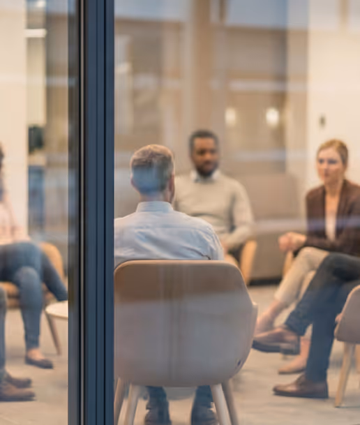 Group of people sitting in a circle inside a room, engaged in a discussion or meeting.