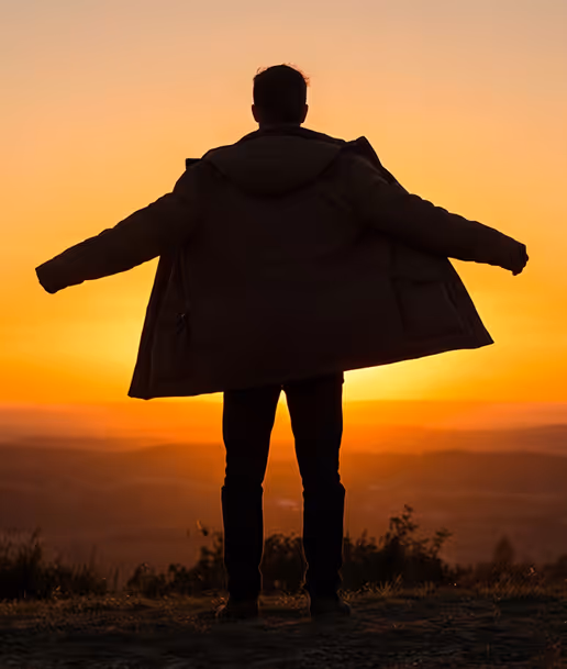 Silhouette of a person spreading their coat wide open standing outdoors during sunset.