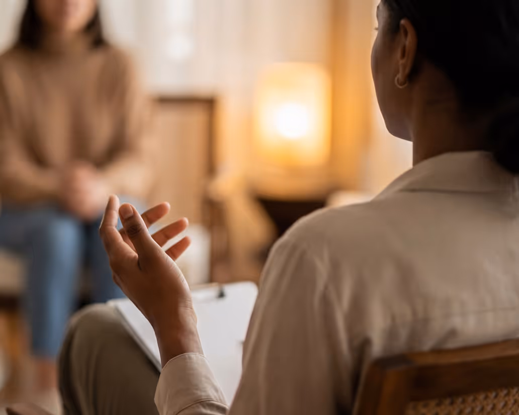 Therapist gesturing with hand while talking to a woman seated across in a warmly lit room.