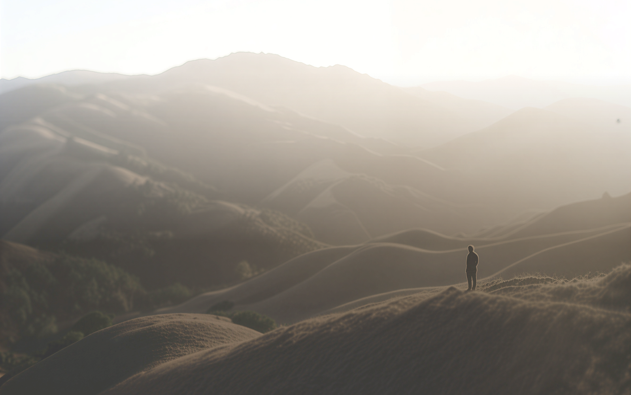 Silhouette of a person standing on a hilltop overlooking rolling hills at sunset.