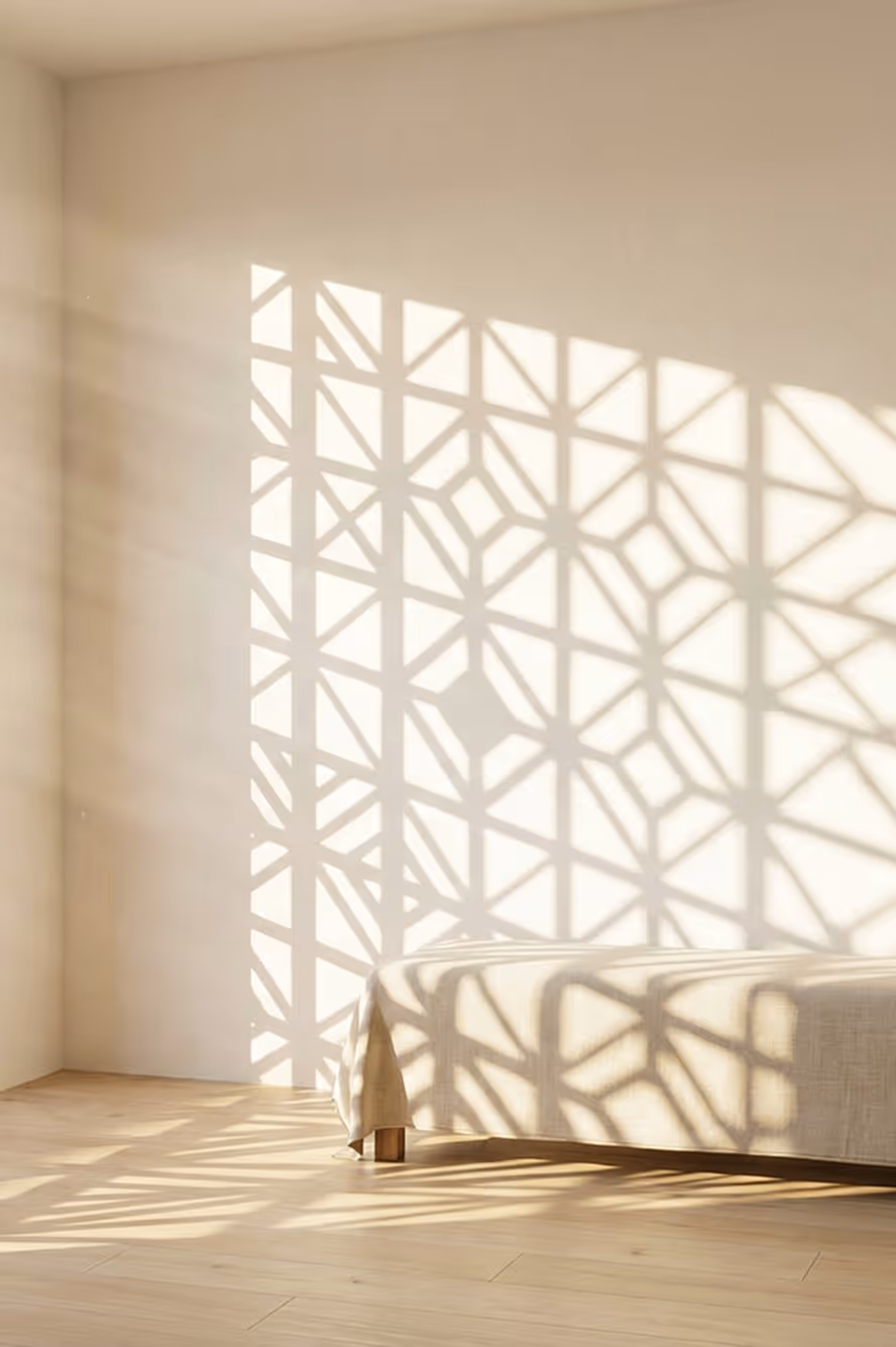 Sunlight casting geometric lattice shadows on a beige wall, floor, and bed with a light-colored cover.