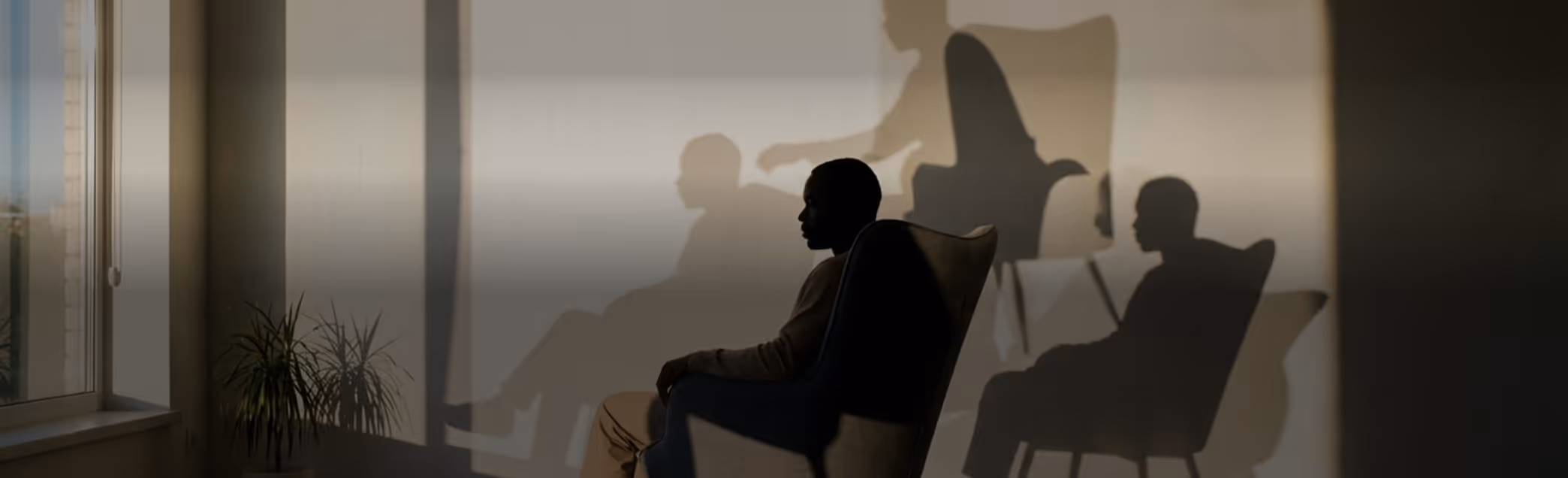 Silhouette of two people seated in chairs with their shadows cast on a wall in a dimly lit room.