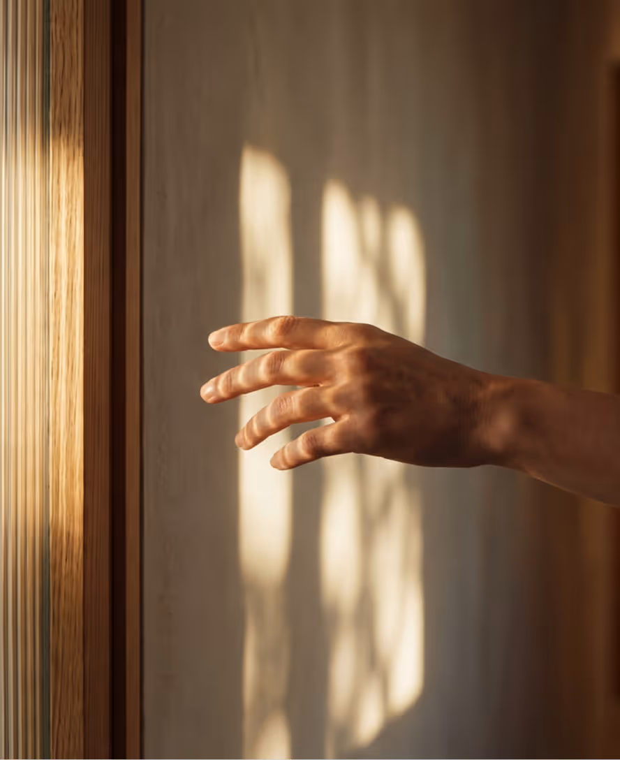 A hand reaching out with sunlight casting window shadows on a beige wall in the background.
