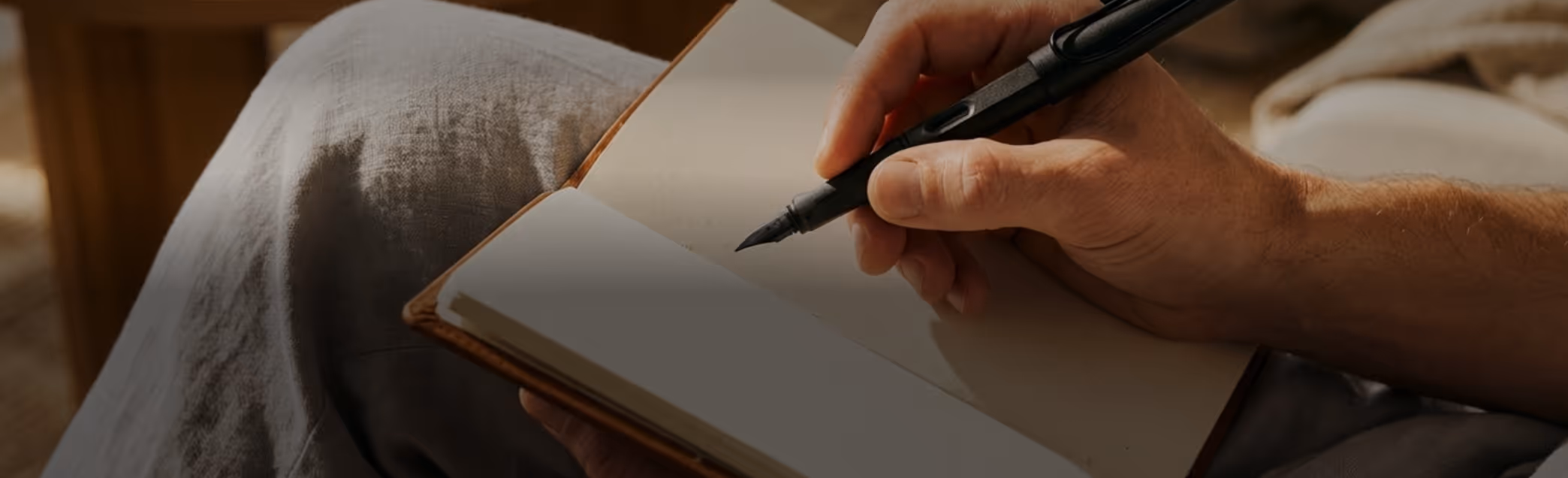 Person holding a fountain pen poised to write in a blank notebook on their lap.