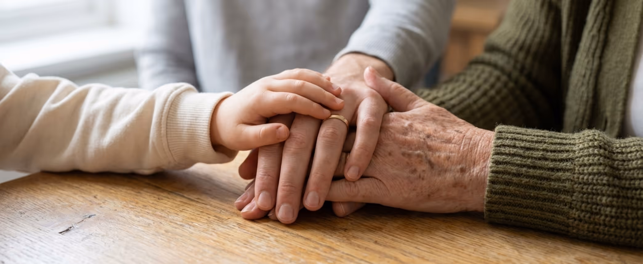 Three generations of hands stacked on a wooden table indicating family support and connection.