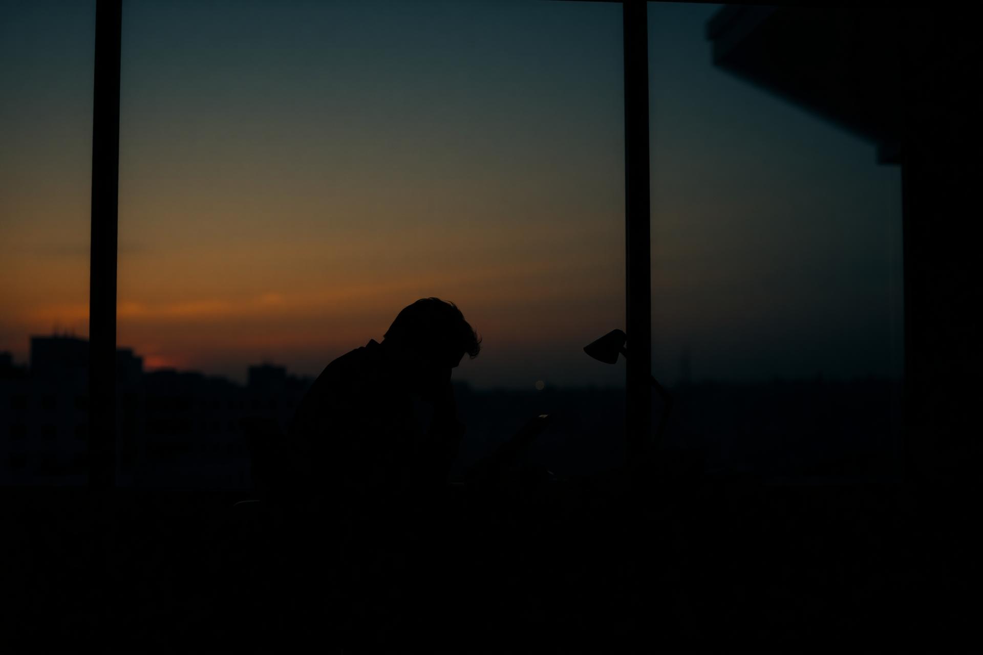 A professional pausing at dusk, quietly weighed down by demanding work