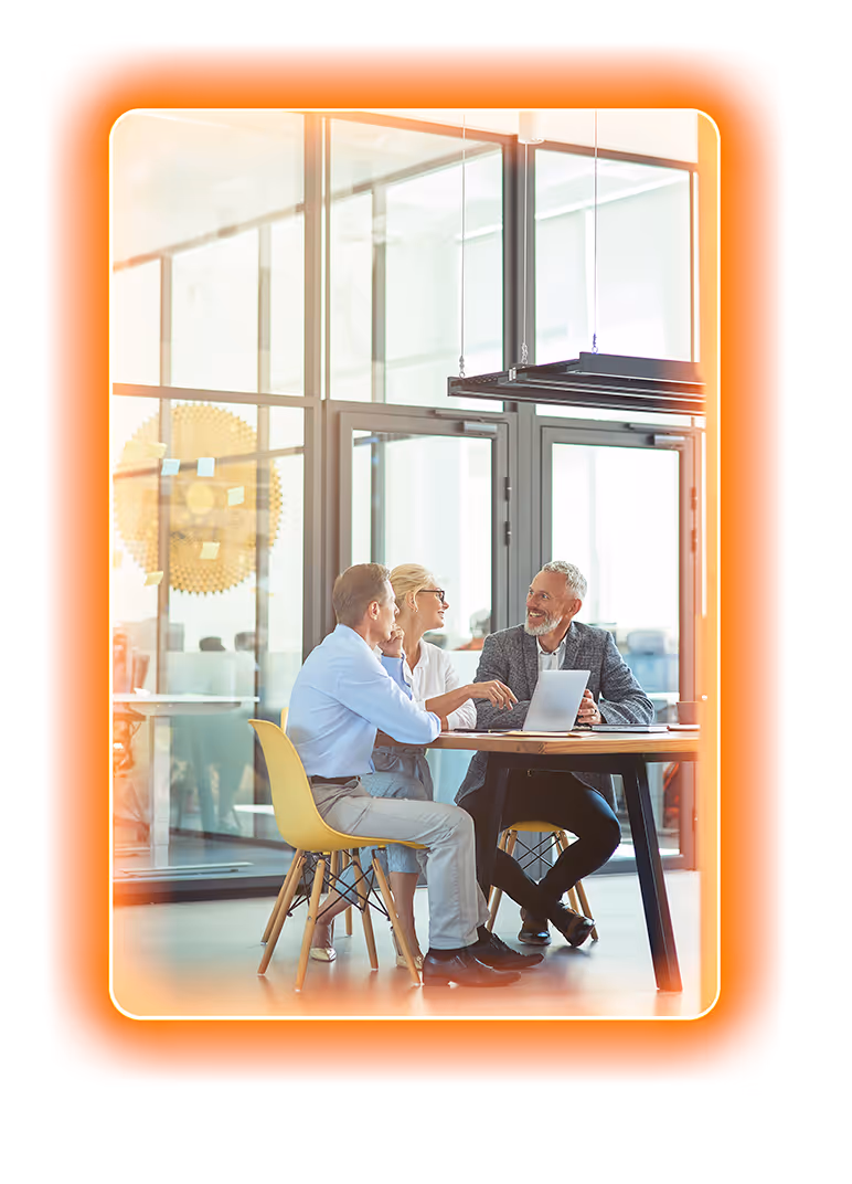 Three business professionals sitting at a round table engaged in a discussion with a laptop in a modern office.