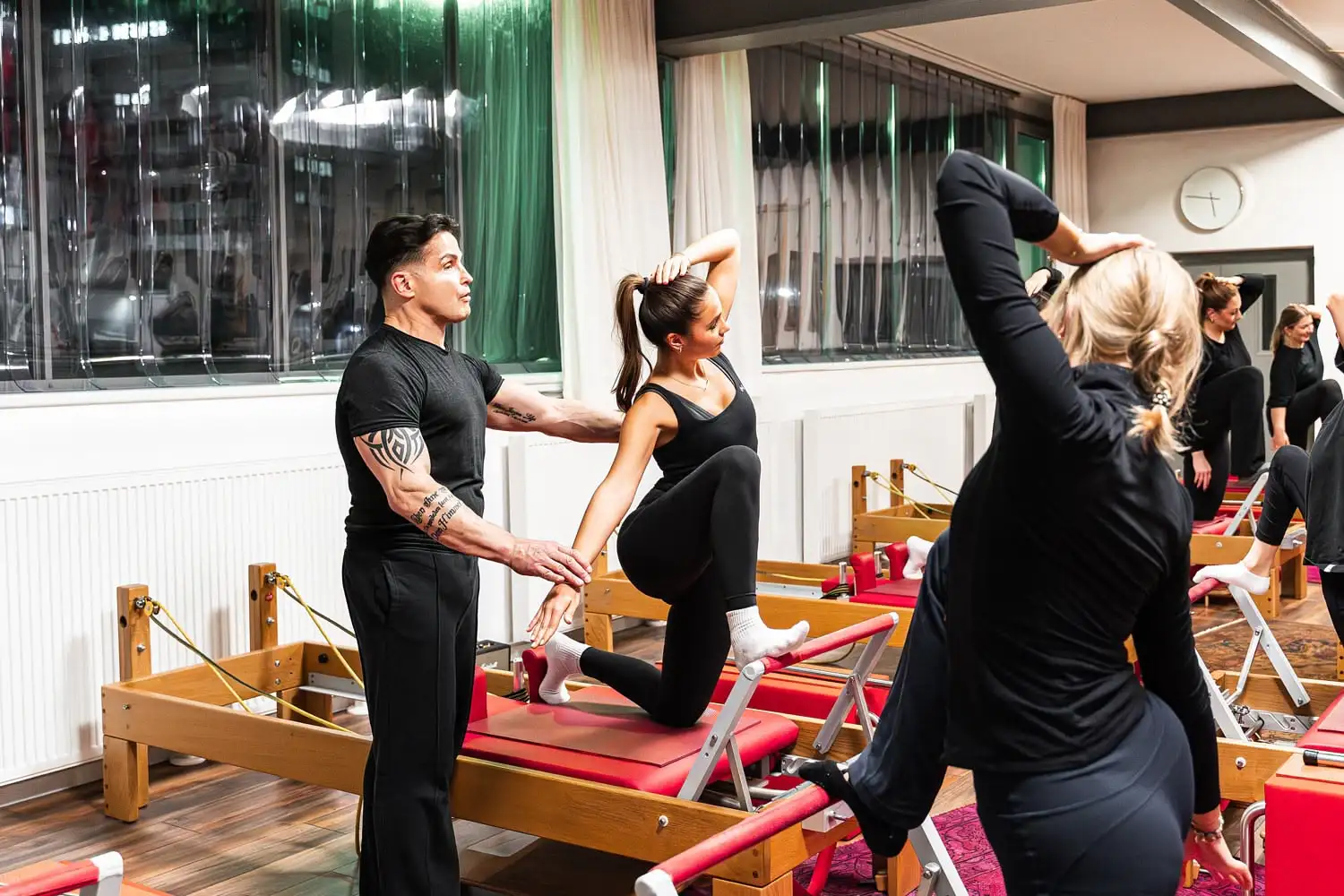 Pilates-Trainer korrigiert Haltung einer Frau während einer Übung auf einem Reformer-Gerät im Studio.