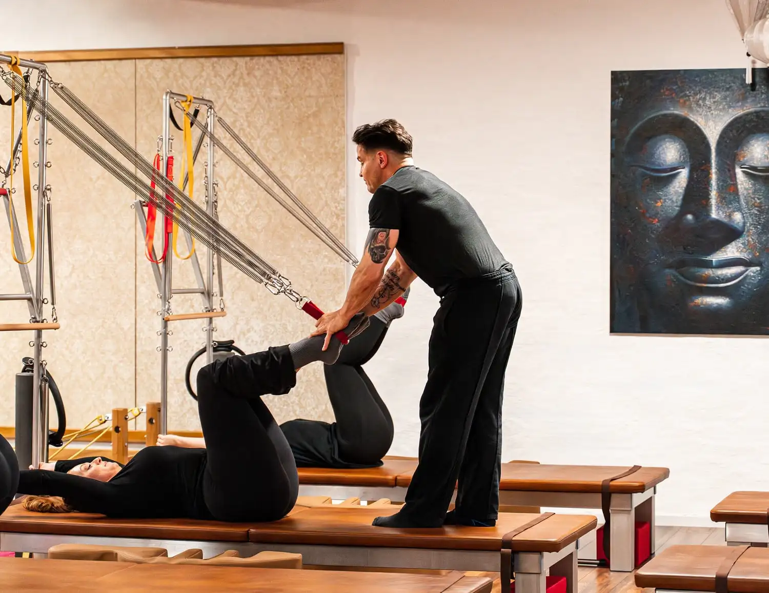 Pilates-Trainer unterstützt eine Frau bei einer Beinübung an Pilates-Gerät Wall Unit (Matte) im hellen Pilates Studio in Hannover