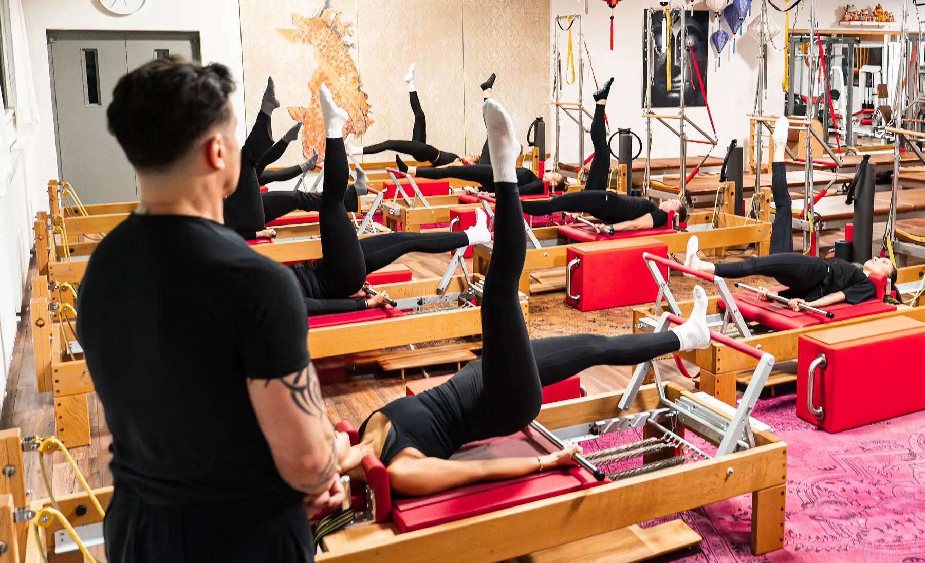 Mehrere Personen führen Pilates-Übungen auf Reformer-Geräten in einem Pilates Studio in Hannover durch, während ein Pilates Trainer zusieht.