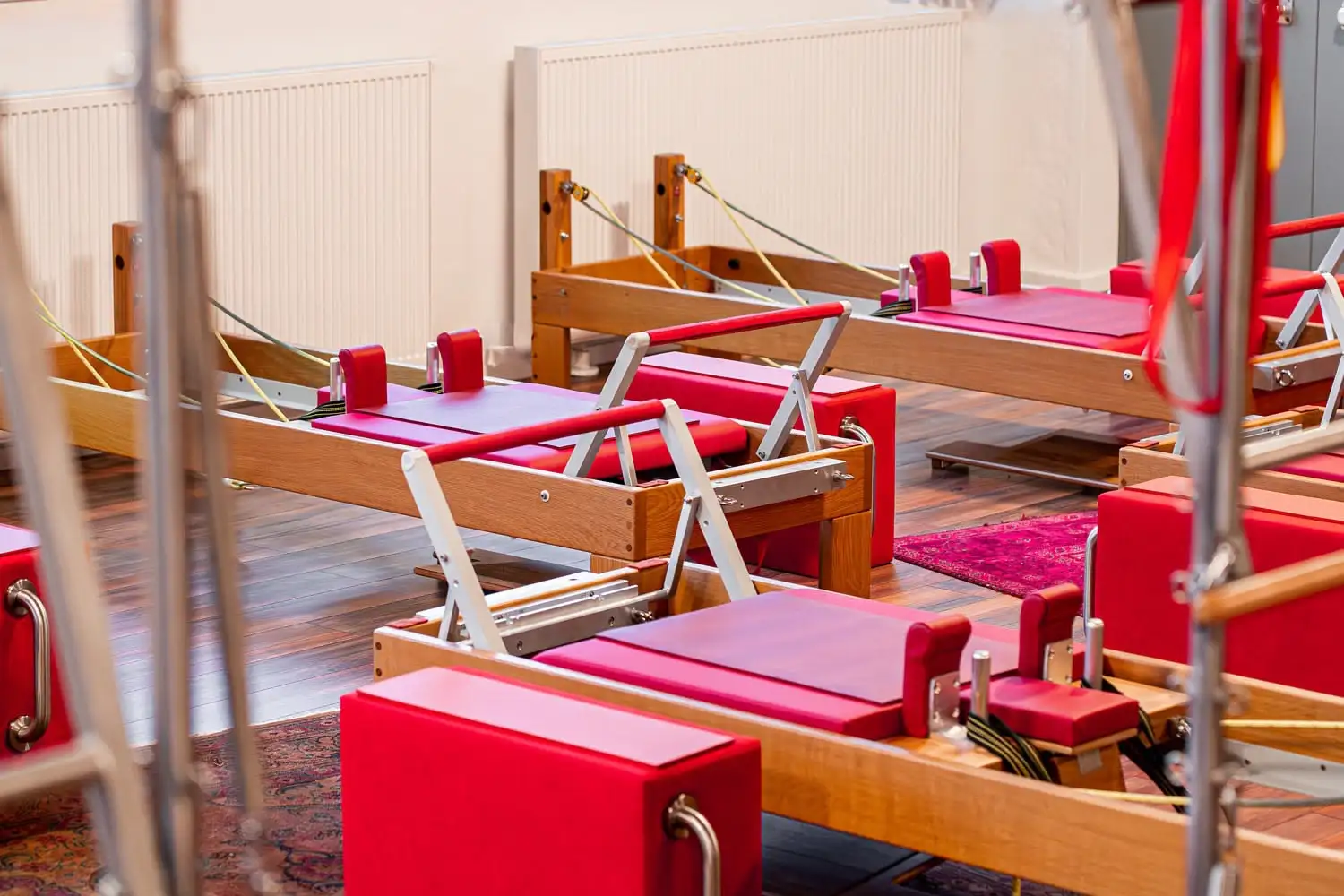 Pilates-Reformer-Geräte mit roten Polstern in einem hellen Pilates Studio Hannover mit Holzboden und weißen Wänden.