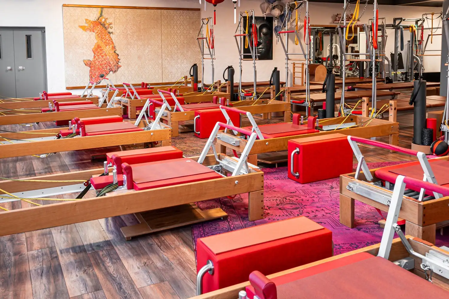 Pilates-Studio Hannover mit mehreren Reformern mit roten Polstern und Wall Unit (Matte) auf Holzfußboden, dekoriert mit asiatischer Kunst.