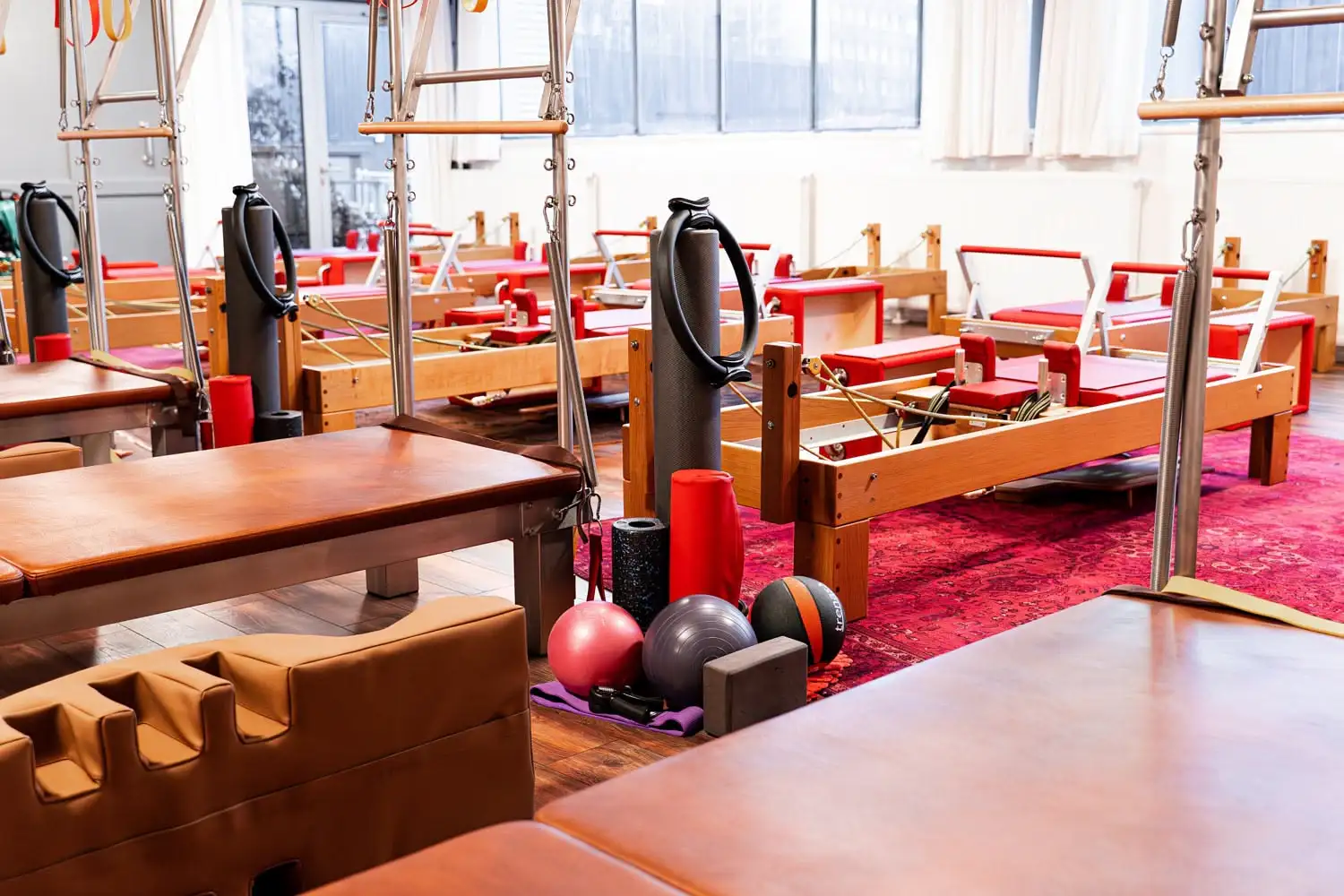 Helles Pilates-Studio in Hannover mit Wall Unit (Matte), Reformer und verschiedenen Trainingsbällen auf einem roten Teppich.