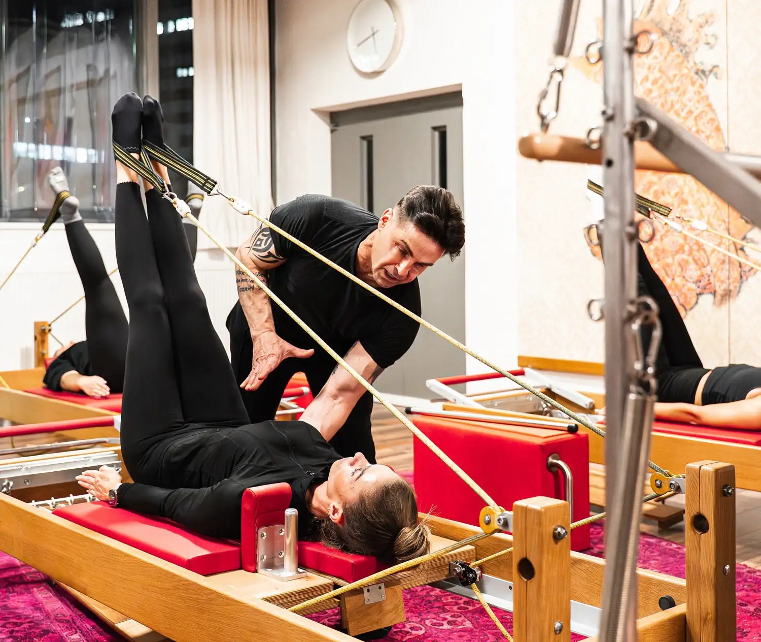 Pilates Trainer korrigiert Haltung einer Teilnehmerin bei Pilates-Übung auf dem Reformer im hellen Pilates Studio