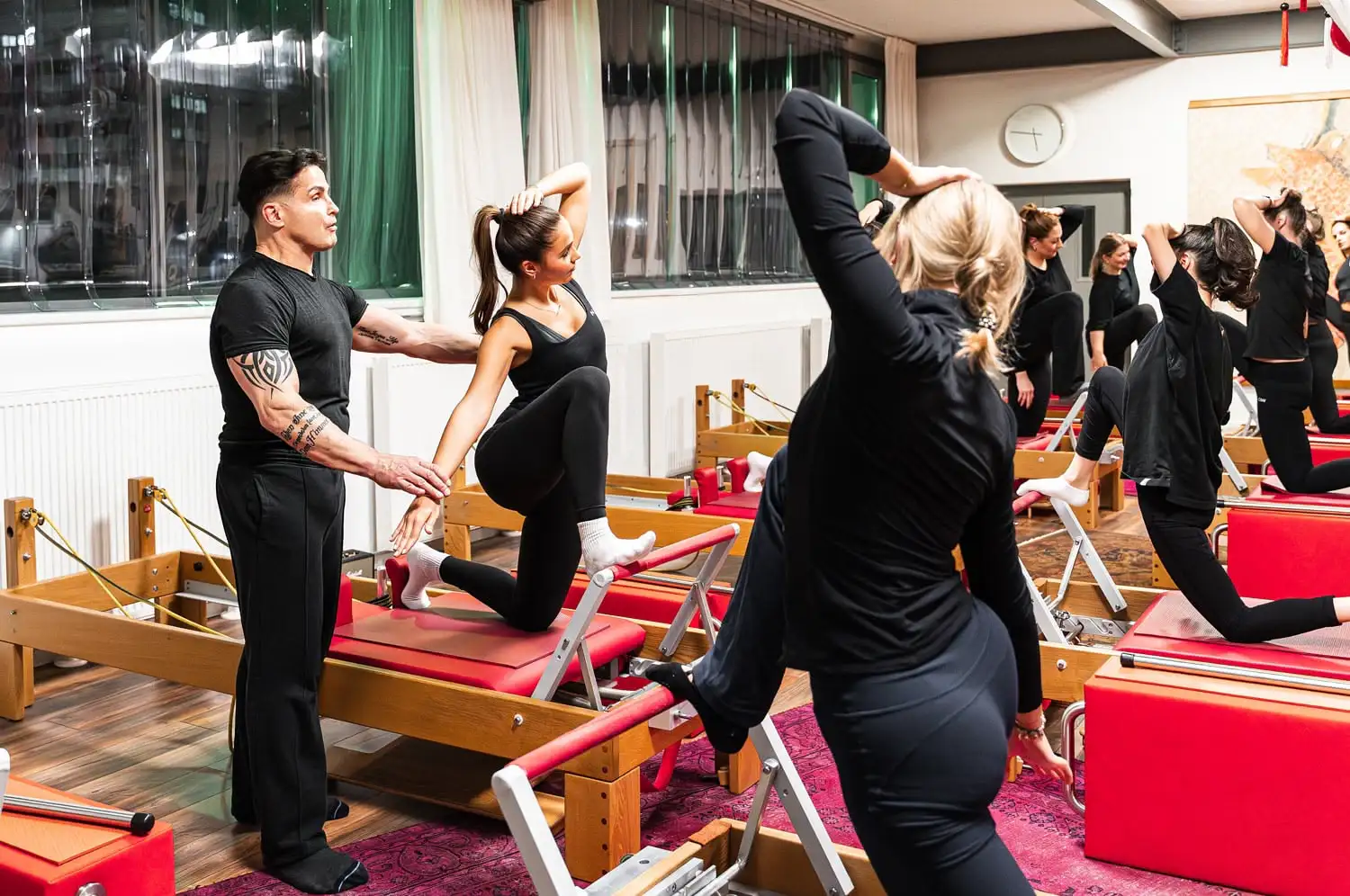 Pilates Studio in Hannover mit Pilates Trainer, der einer Frau bei einer Übung auf dem Reformer-Gerät hilft, andere Teilnehmer machen gleiche Übung.