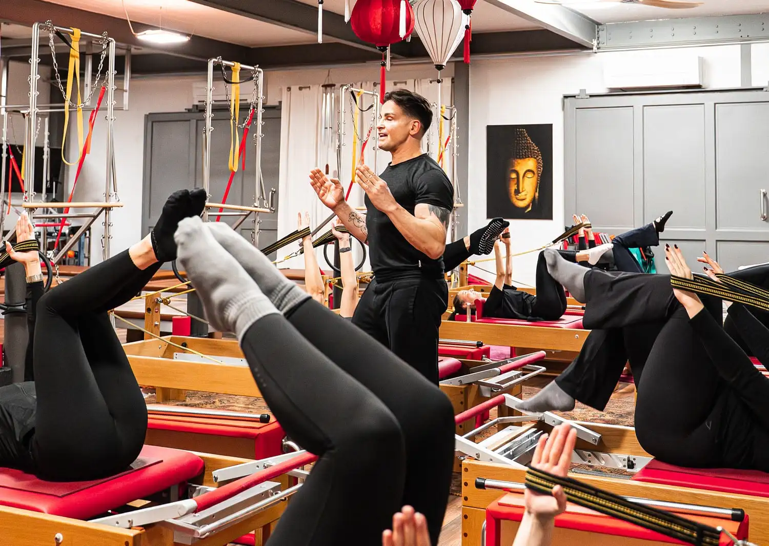 Pilates-Kurs mit einem Pilates Trainer, der mehrere Personen auf Reformern anleitet, die Beine und Arme gestreckt heben.