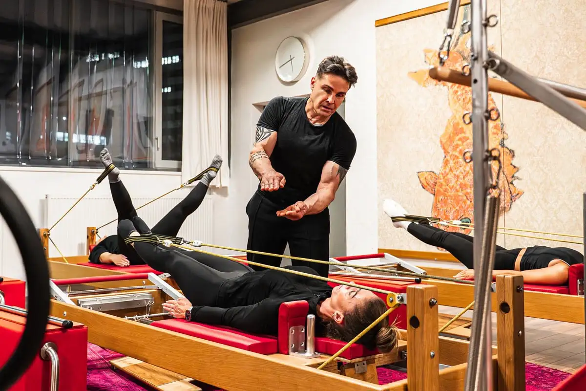 Pilates-Trainer korrigiert Frau bei einer Übung auf dem Reformer-Gerät in einem Pilates Studio in Hannover