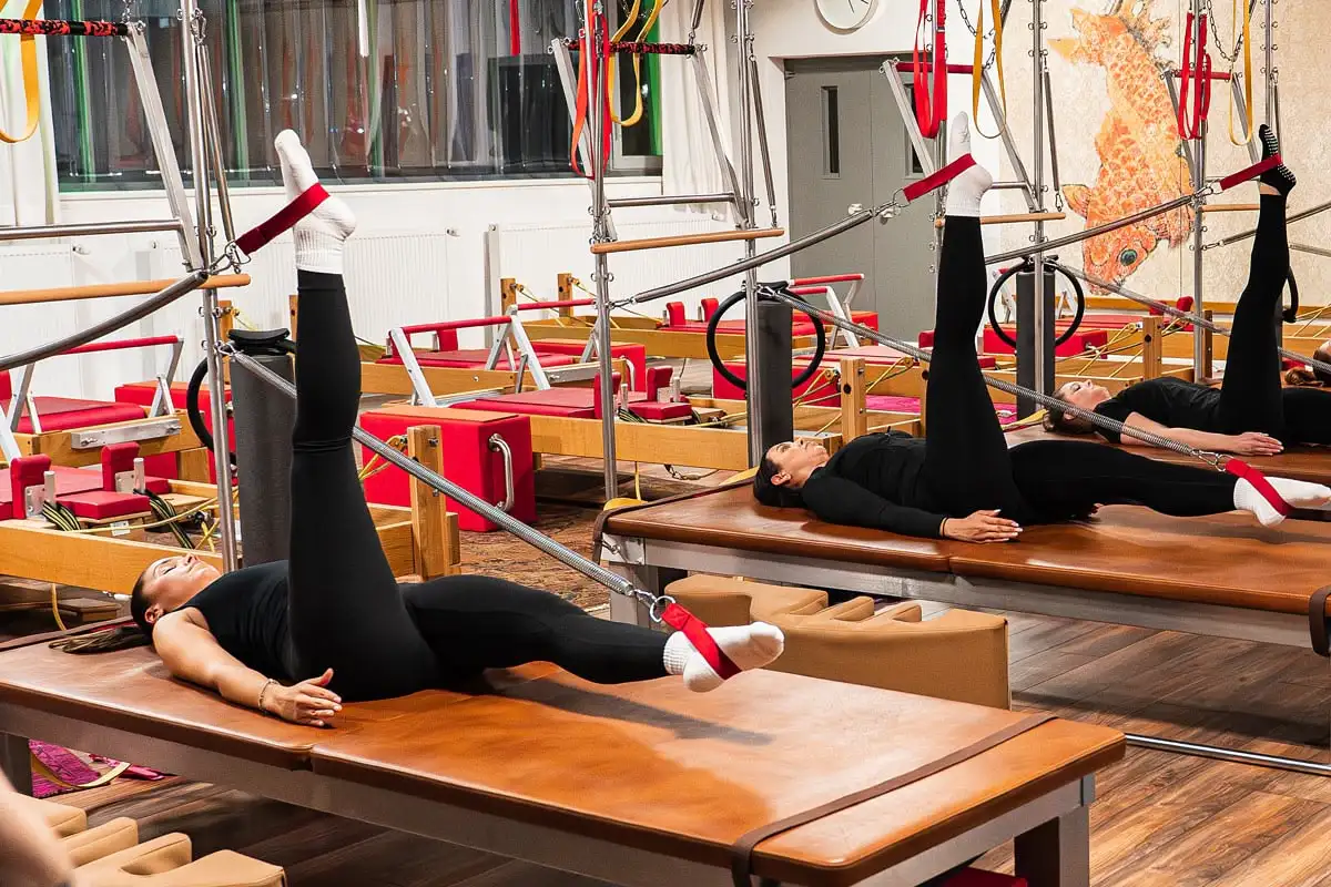 Frau in schwarzer Sportkleidung macht Pilates-Übungen auf einem Reformer mit Fußschlaufen in einem Pilates Studio Hannover