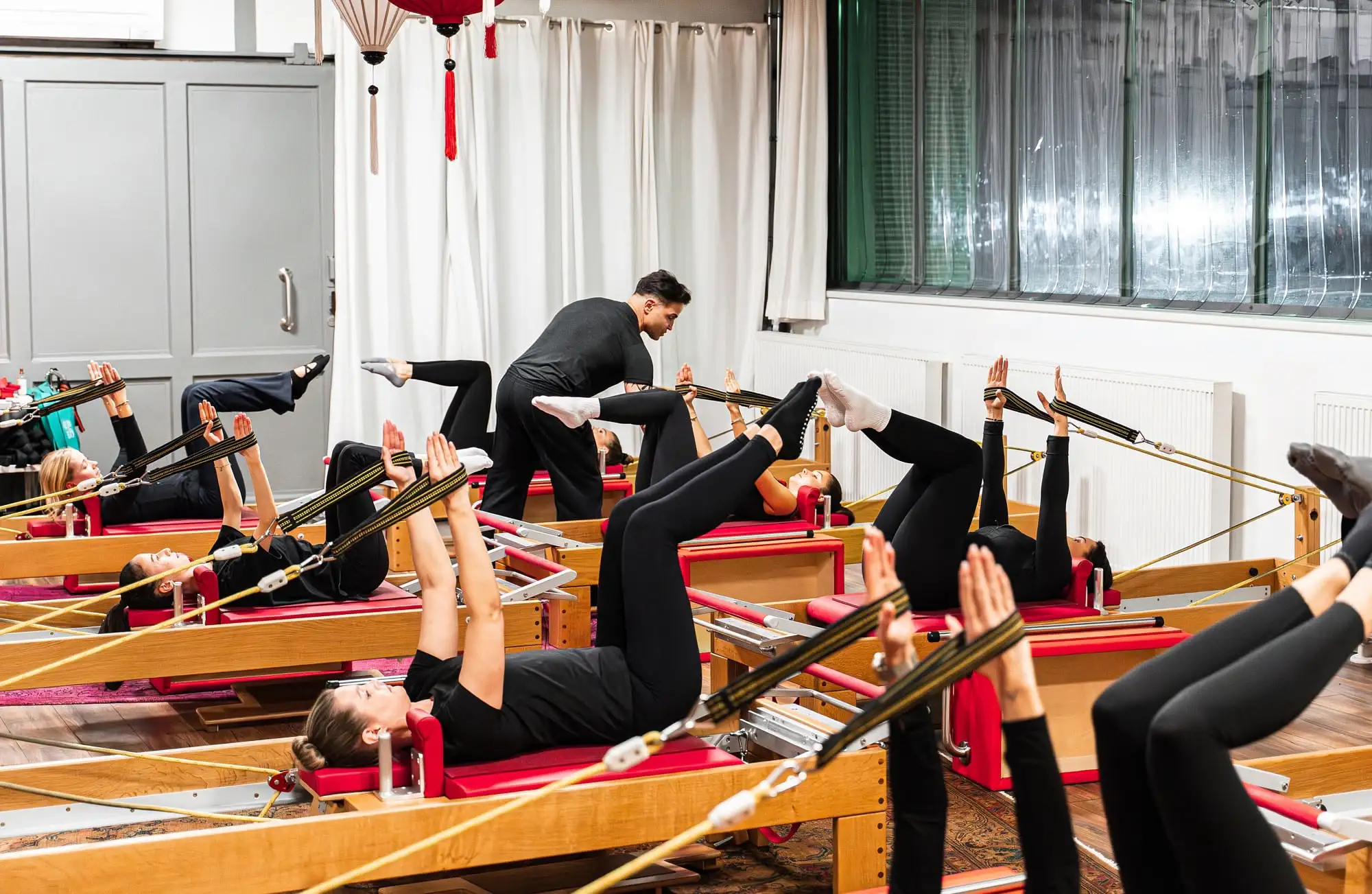 Mehrere Personen machen Pilates mit Widerstandsbändern auf Reformer-Geräten in einem Pilates Studio Hannover, betreut von einem Pilates Trainer.