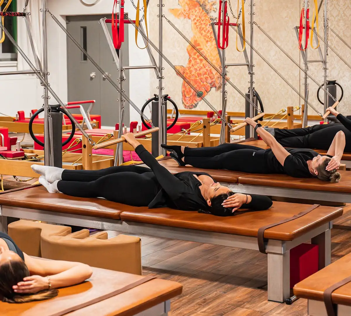 Mehrere Frauen in schwarzer Sportkleidung liegen auf Pilates Wall Unit