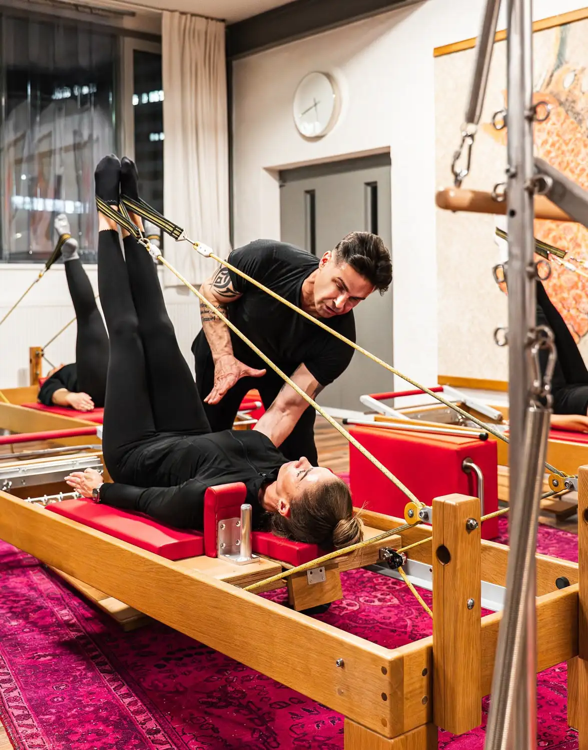 Pilates-Trainer korrigiert eine Frau, die Übungen auf einem Reformer-Gerät macht.