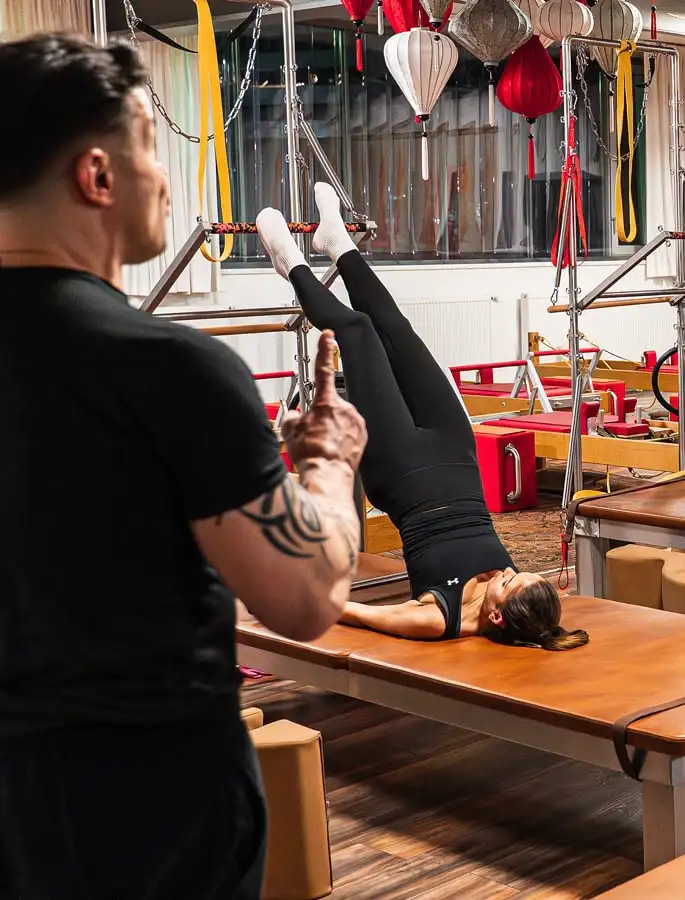 Frau im Pilates Studio in Hannover macht Pilates-Übung auf einer Wall Unit, während ein Pilates Trainer sie beobachtet.