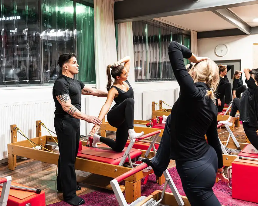 Pilates-Trainer korrigiert Haltung einer Frau während einer Übung auf einem Reformer-Gerät im Studio.