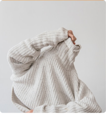 Person wearing a light gray ribbed knit sweater with long sleeves and a high collar.