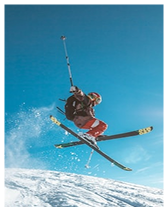 Skier in mid-air performing a jump on snow-covered slope against a clear blue sky.