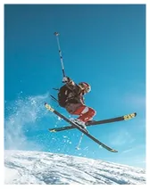 Skier in mid-air performing a jump on snow-covered slope against a clear blue sky.