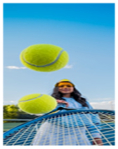 Young woman hitting a tennis ball with a racket against a blue sky.
