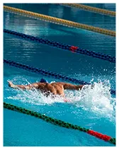 Swimmer performing butterfly stroke in a lane of an outdoor swimming pool with splashing water.