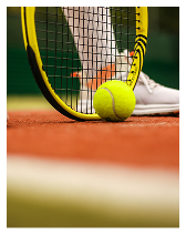 Close-up of a tennis ball and racket on a clay tennis court near a player's foot.