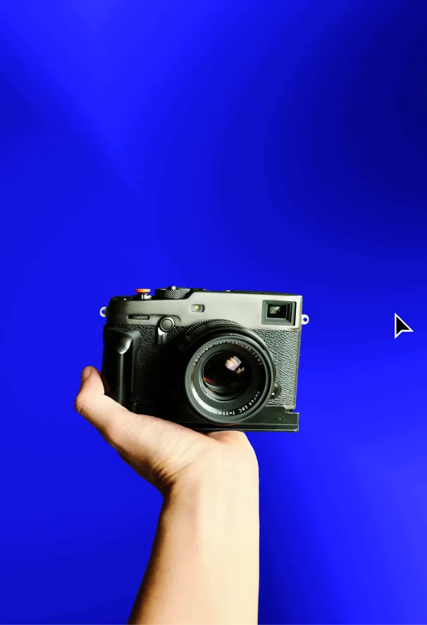 Hand holding a black vintage-style camera against a solid bright blue background.