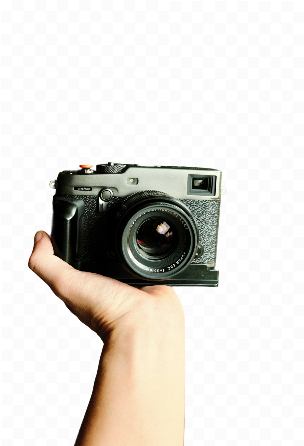 Hand holding a black digital camera facing forward with visible lens and controls.