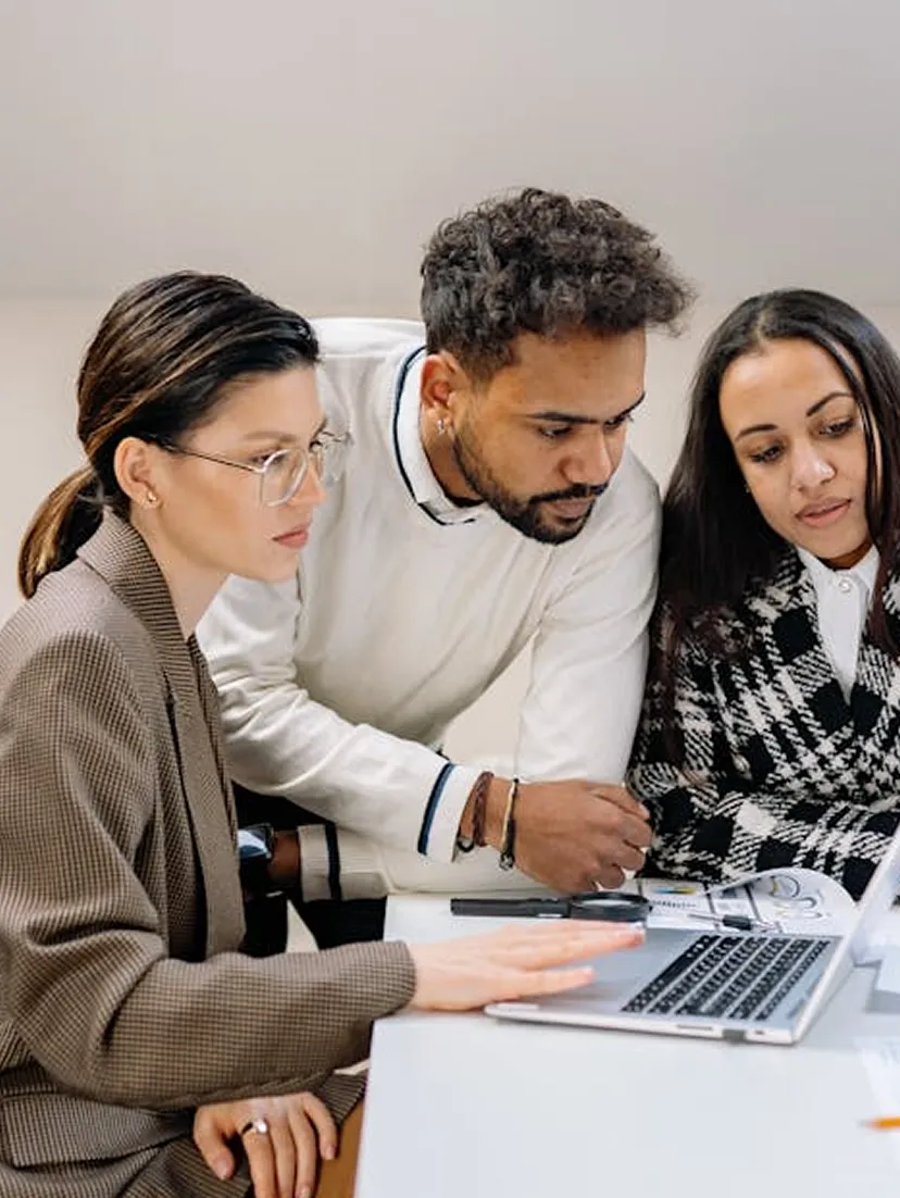 Three professionals, two women and one man, intently reviewing information on a laptop at a white desk.