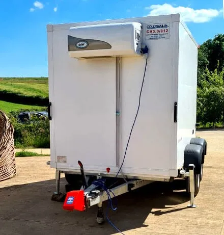 White refrigerated trailer with cooling unit and hitch, parked on a paved surface outdoors.
