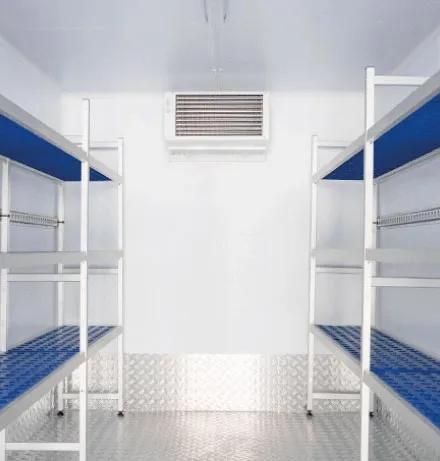 Interior of a clean refrigerated trailer with metal shelving on both sides and an air cooling unit mounted on the back wall.