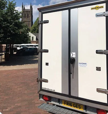 Rear view of a white refrigerated delivery truck parked on a brick street with a tall church tower in the background.