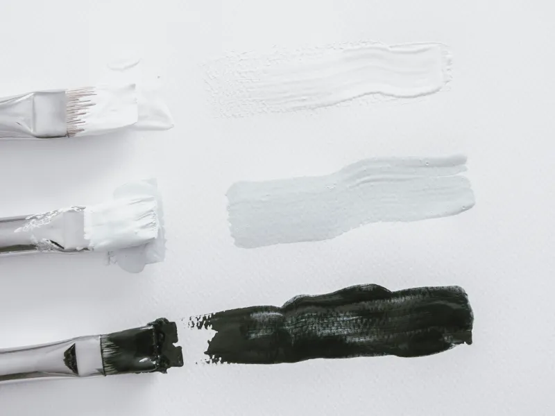 Drie kwasten met witte, lichtgrijze en donkergrijze verfstreken op een witte achtergrond