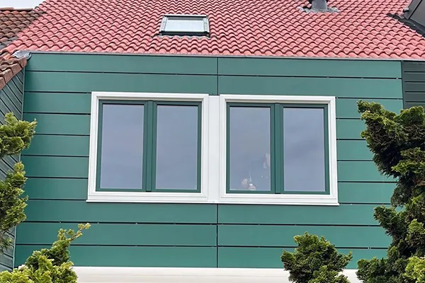Groene kunststof gevelbekleding met twee witte kozijnen op de eerste verdieping van een woning met rood pannendak