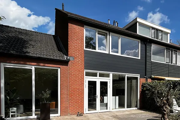 Woning met kunststof kozijnen, witte schuifdeuren en donkergrijze gevelbekleding, gezien vanaf de tuin