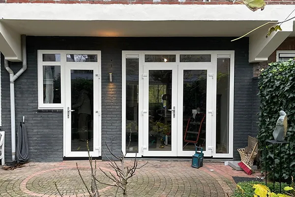 Achtergevel met witte kunststof deuren en kozijnen in een donkergrijze muur, uitkijkend op een tuin met bestrating