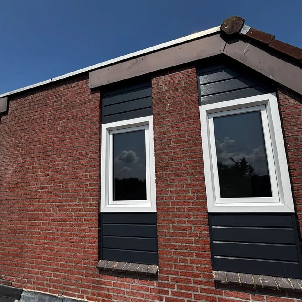 Rode bakstenen gevel met twee wit omlijste ramen en donkere gevelbekleding onder een puntdak