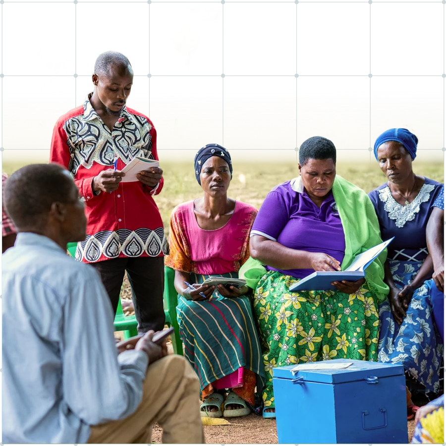 Group of five people, with four seated and one standing, engaged in reading and discussion outdoors around a blue box.