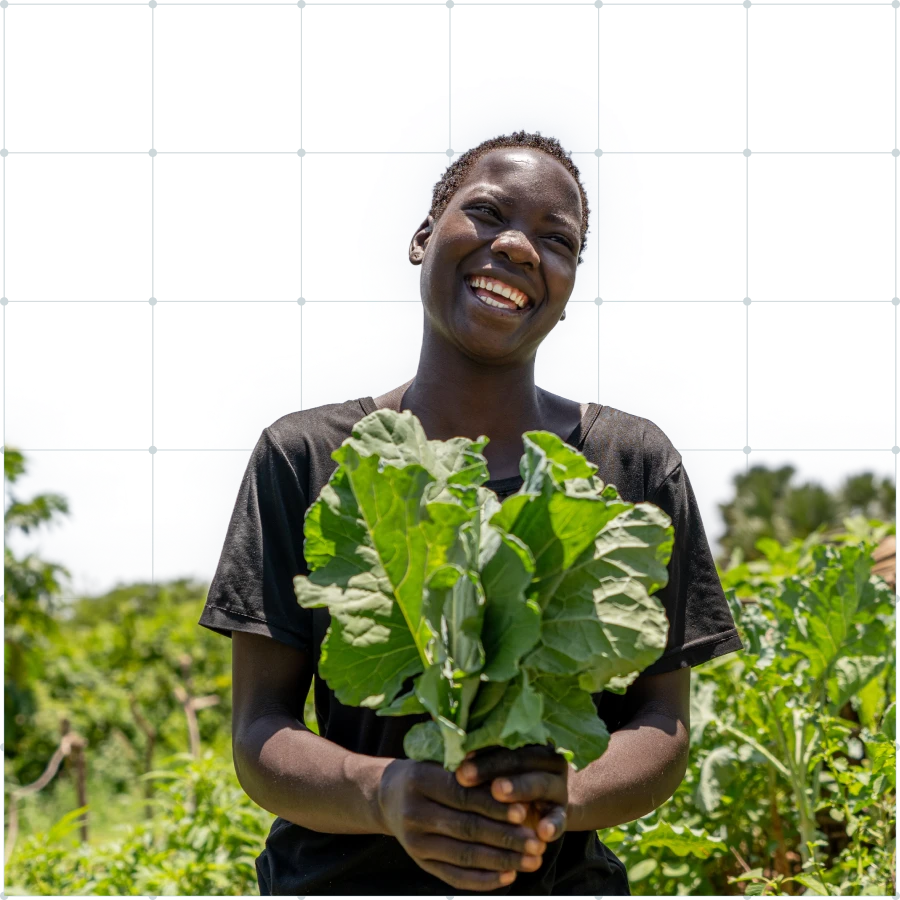 A farmer tending to tall green bean plants supported by wooden stakes in a lush field under a cloudy sky.