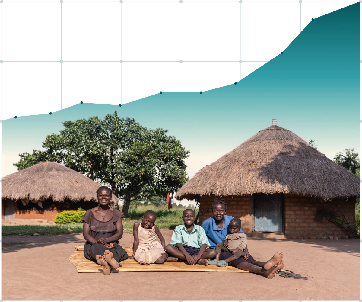 Healthcare workers in pink and white coats consult with women sitting in plastic chairs outside a rural building, with medical supplies on the table.