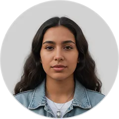 Retrato de una mujer joven con cabello largo y rizado, con chaqueta de mezclilla y collar, sobre fondo gris claro.