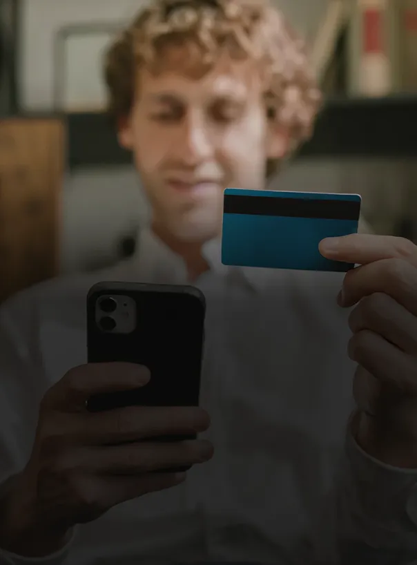 Hombre sosteniendo un teléfono móvil y una tarjeta de crédito azul mientras sonríe.